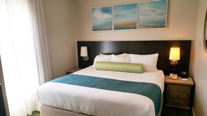 A hotel room with a large bed, two bedside tables, a nightstand, a lamp, and three paintings on the wall. - 1 bdrm sleeps 6 with hall bunks (Miramar Beach)