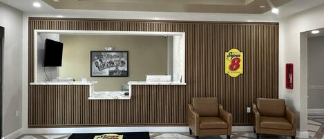 A reception area with a wooden panel wall, a reception desk, two brown chairs, a black and yellow mat, and a 'Super 8' sign.