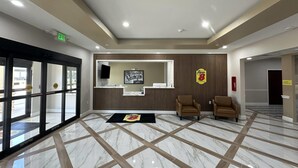 Un hall de hotel con mostrador de recepción, dos sillones, piso con diseño y una entrada con puerta de vidrio grande.