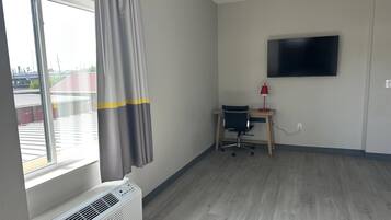 Quarto com uma janela grande, uma escrivaninha com cadeira, televisão de tela plana e abajur vermelho.