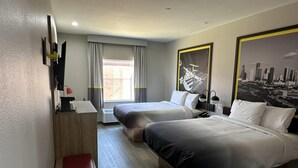 Ein Hotelzimmer mit zwei Betten, einem Schreibtisch, einer Bank, einem Fernseher und einem großen Stadtplakats.