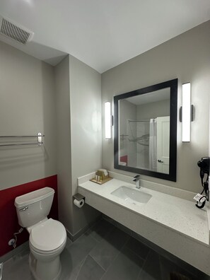 Une salle de bain moderne équipée d’un WC, d’un lavabo, d’un miroir, d’un porte-serviettes et d’un sèche-cheveux.