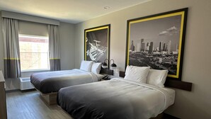 Habitación de hotel con dos camas, una ventana con cortinas, un cuadro de un paisaje urbano y una lámpara fijada a la pared.