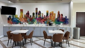 Eine moderne Küche mit einem großen, farbenfrohen Stadtbild-Wandgemälde, einem Flachbildfernseher und einem Essbereich mit braunen Stühlen und einem weißen Tisch.