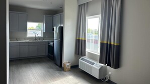 Una cocina moderna con armarios grises, refrigerador empotrado, ventana con cortinas y aire acondicionado de pared.