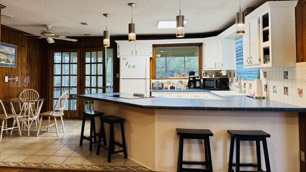 A kitchen with a large island, bar stools, a refrigerator, and a window with a view of trees. - The Fish Cottage - south beach, lots of amenities (Tybee Island)