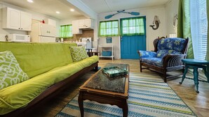 A living room with a sofa, a chair, a coffee table, and a kitchen area with cabinets and a microwave. - The Fish Cottage - south beach, lots of amenities (Tybee Island)