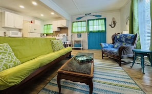 A living room with a sofa, a chair, a coffee table, and a kitchen area with cabinets and a microwave. - The Fish Cottage - south beach, lots of amenities (Tybee Island)