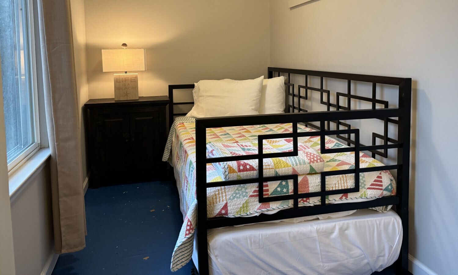 A bunk bed with a colorful quilt, a bedside table with a lamp, and a window with curtains.