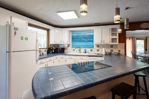 A kitchen with a large island, white cabinets, a painting of the ocean, and pendant lighting. - Red Fish - close to beach, lots of amenities (Tybee Island)