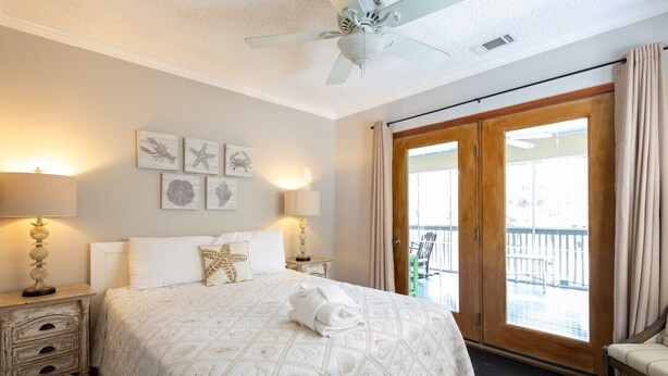 Un dormitorio con una cama grande, ventilador de techo, balcón con vistas y obras de arte en la pared.