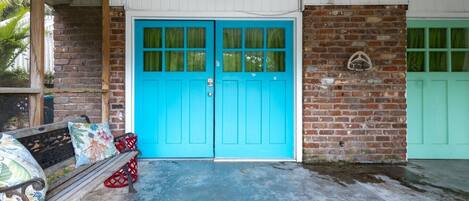 A building entrance with a blue door, a brick wall, and a bench with cushions.