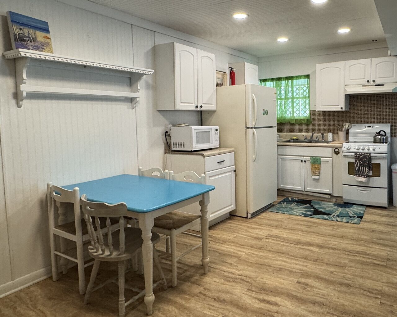 A compact kitchen with white cabinetry, a blue table, and a microwave.