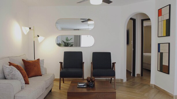 Ein modernes Wohnzimmer mit einer Couch, zwei Sesseln, einem Couchtisch und einem Deckenventilator.