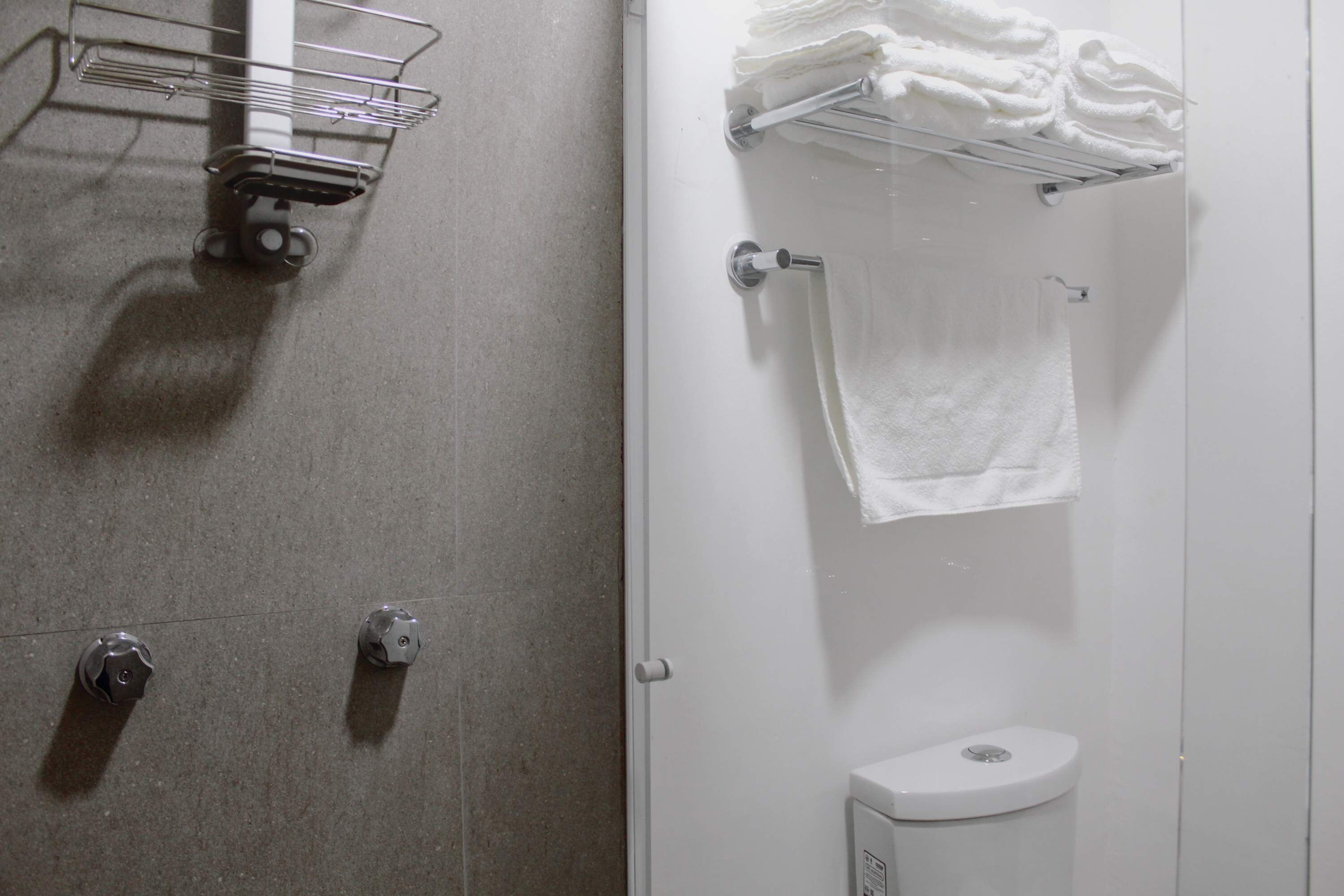 A bathroom with a shower, a toilet, and a towel rack with folded towels.