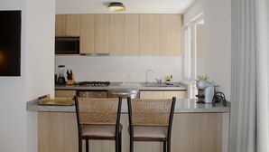 Eine moderne Küche mit Holzschränken, einer Granitabdeckung, zwei Korbstühlen und einer kleinen Kochinsel mit Spüle und Wasserkocher.