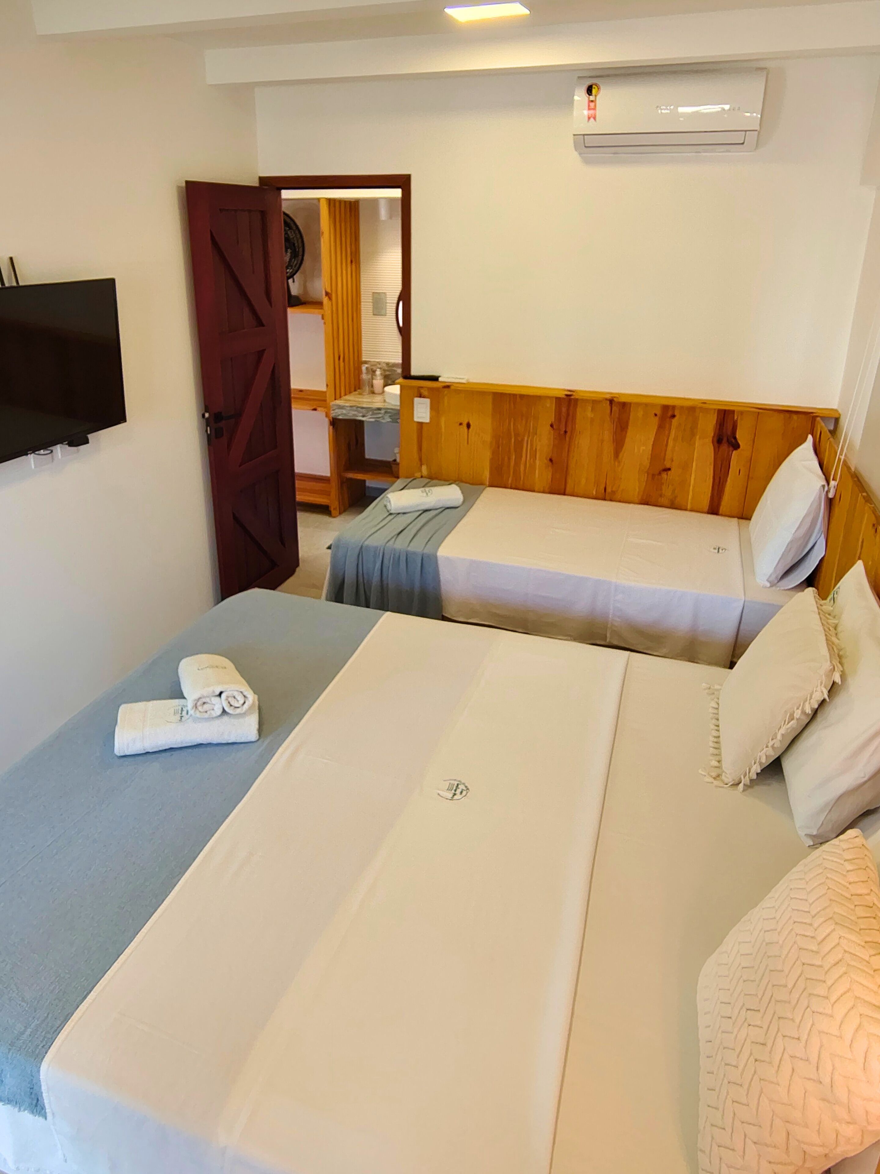 A room with two beds, a TV mounted on the wall, and an air conditioning unit.