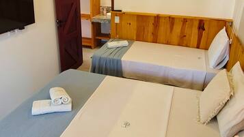 A room with two beds, a TV mounted on the wall, and an air conditioning unit.