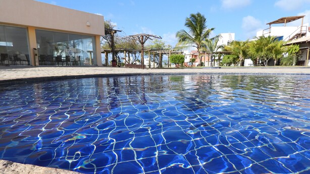 A clear swimming pool with a tiled edge, surrounded by a building with large windows and outdoor seating. - Chalet near the beach, with kitchen and balcony with hammock. Couples and families with children (São Miguel do Gostoso)