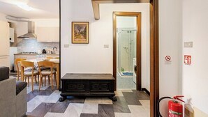 A modern kitchen with a dining area, a fireplace, and a hallway leading to a bathroom. - MV - Three-room apartment, covered garage 15 minutes from downtown (Trieste)