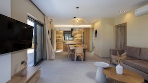 Een moderne woonkamer met een flatscreen televisie, een eethoek met een tafel en stoelen, en een bank.