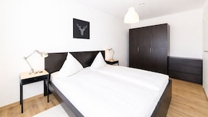 A modern bedroom with a large bed, two bedside tables with lamps, a dark wardrobe, and a framed deer head on the wall. - Ferienresidenz Hinterzarten FEWO H2 (Hinterzarten)