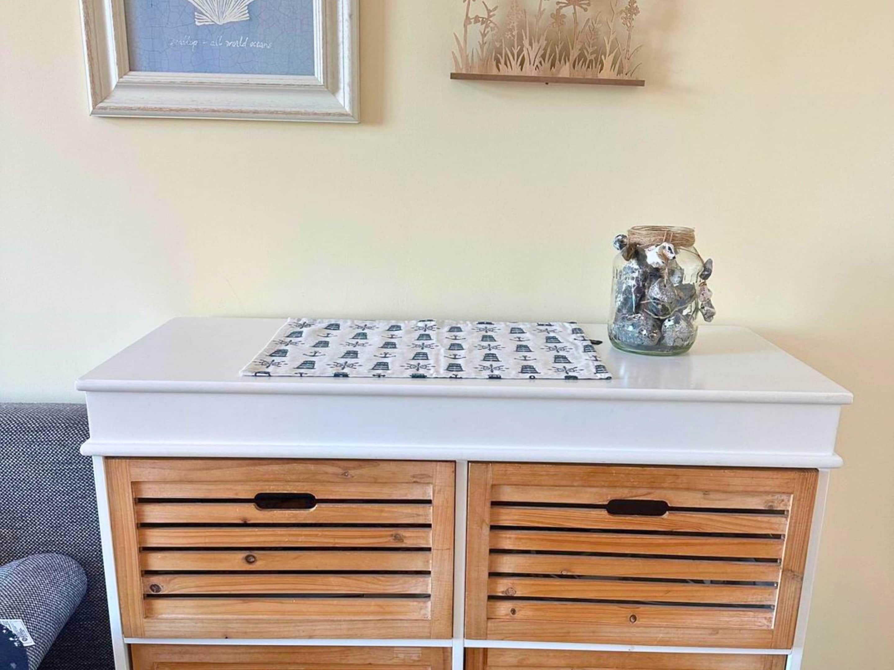 A white table with a patterned cloth, two wooden drawers with handles, and a glass jar with items on top.