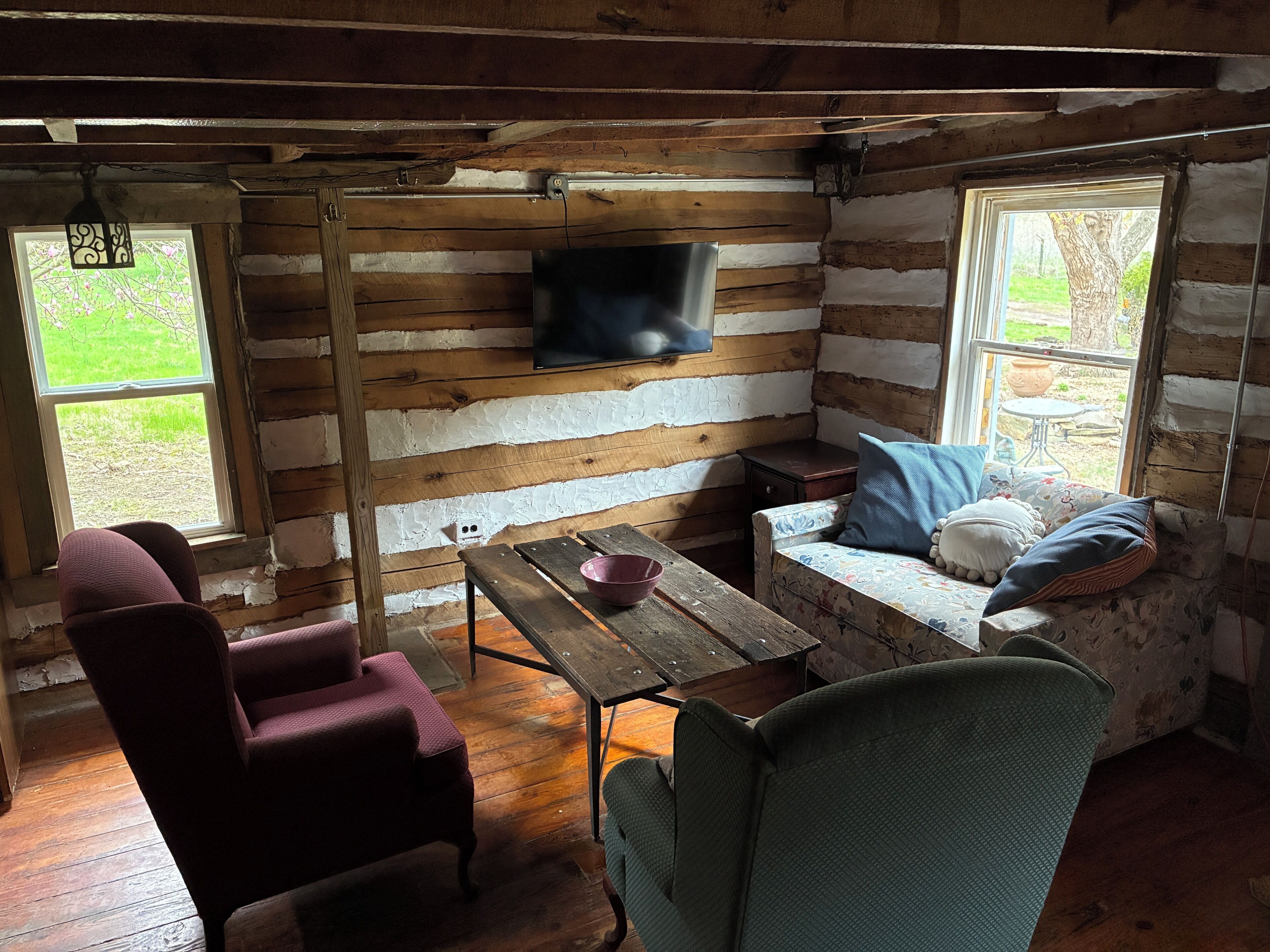 L’intérieur d’un chalet rustique, avec des murs en bois, une table en bois, un canapé avec des coussins et un téléviseur fixé au mur.