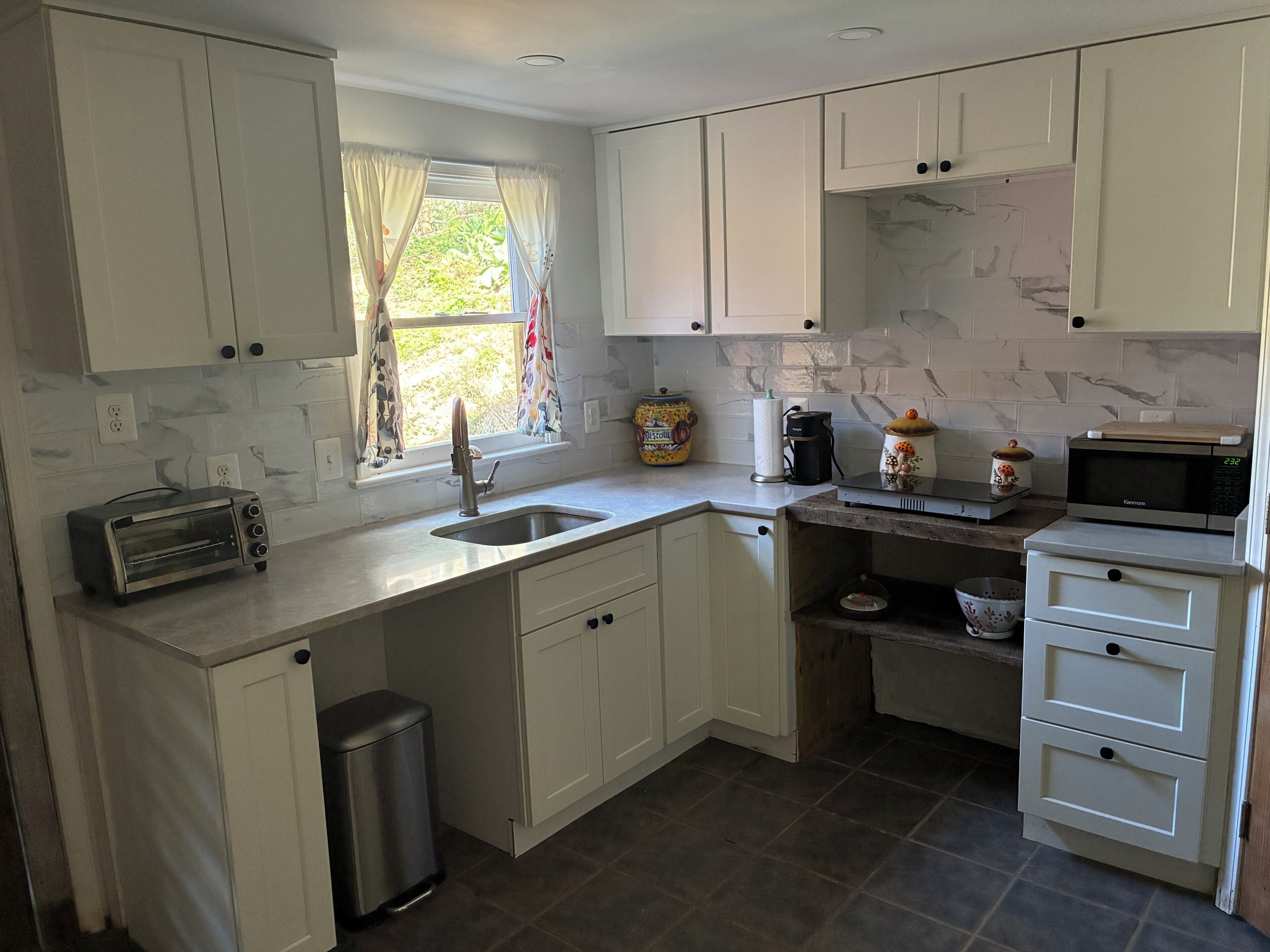 A kitchen with white cabinets, a toaster, a sink, a coffee maker, and a microwave.