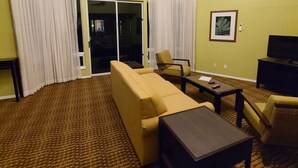 Une chambre d’hôtel équipée d’un canapé, de fauteuils, d’une petite table, d’un téléviseur et d’une porte-fenêtre coulissante.