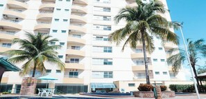 Um hotel com vários andares, varandas, palmeiras e uma piscina.