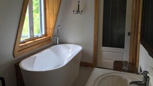Un baño moderno con una bañera independiente, un lavamanos y un ventanal con marco de madera.