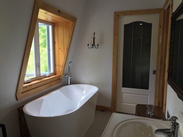 Une salle de bain moderne avec une baignoire sur pieds, un lavabo et une fenêtre avec un cadre en bois.