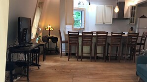 Un espacio habitable amplio con piso de madera, una mesa de comedor con sillas, un televisor y una cocina al fondo.
