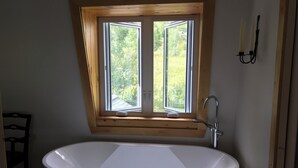 Un baño con una bañera independiente, una ventana sobre la bañera y un aplique en la pared.