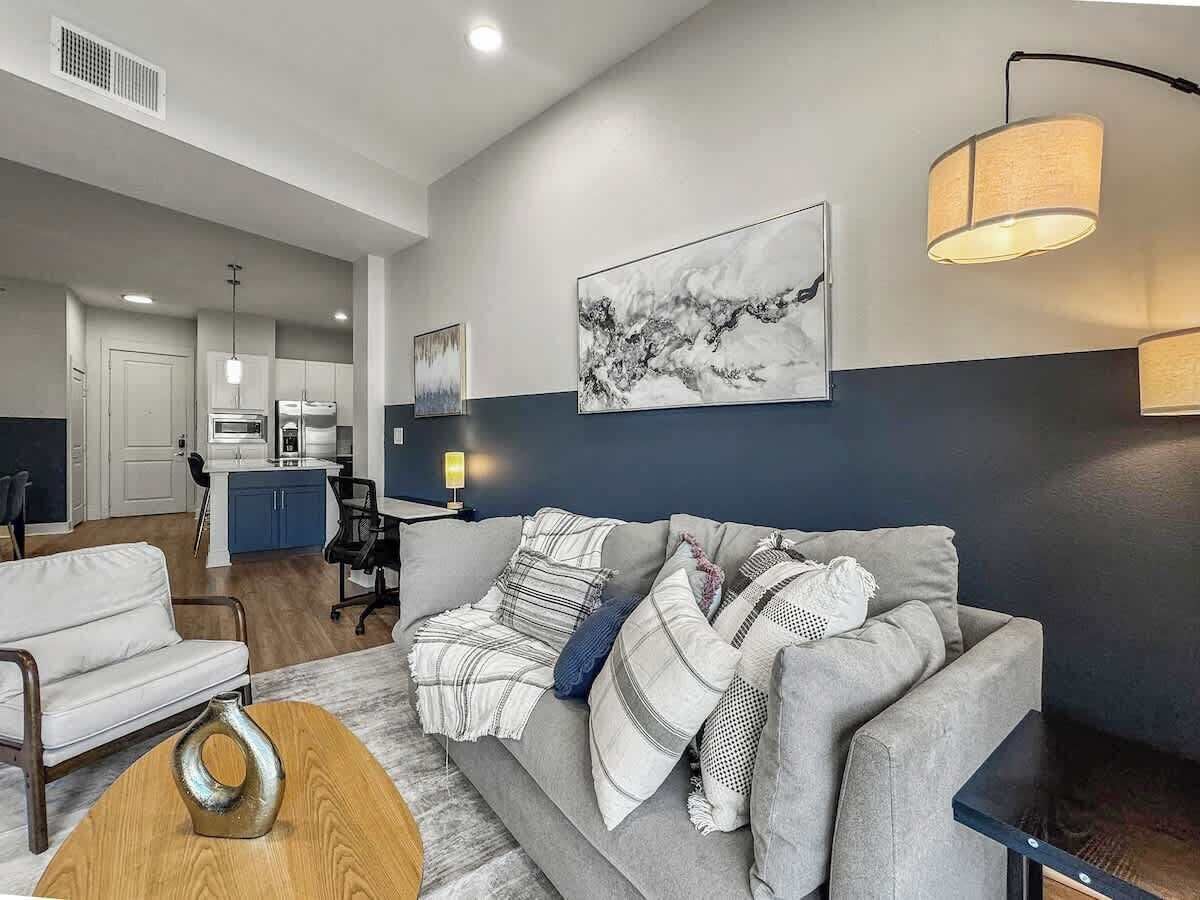 A modern living room with a grey sofa, a wooden coffee table, and a dining area with a kitchen in the background.