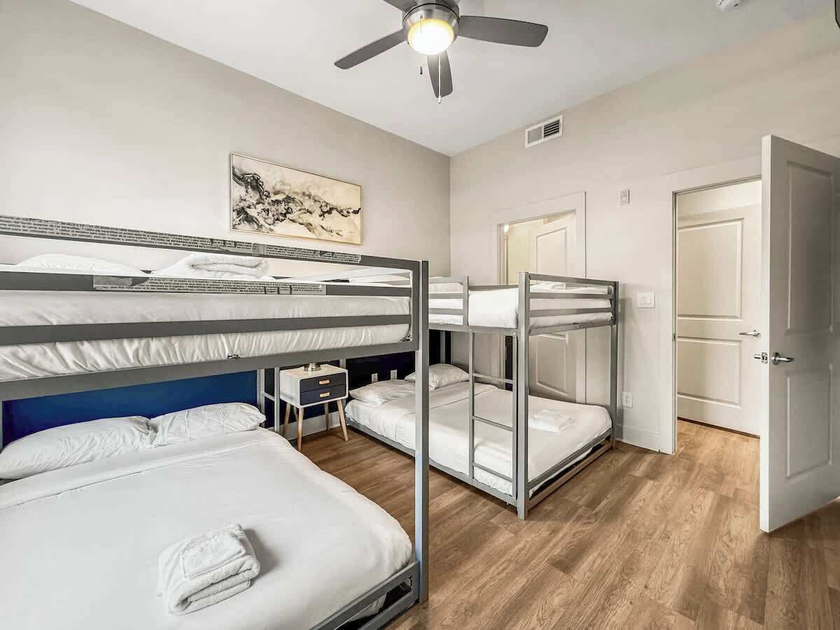 A hotel room with bunk beds, a ceiling fan, a small bedside table, and a door.