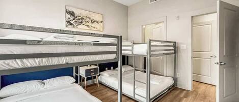 A hotel room with bunk beds, a ceiling fan, a small bedside table, and a door.