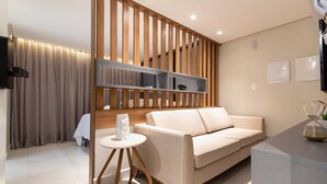A modern living room with a beige sofa, a small round table, and a wooden partition with shelves. - Unity Cabo Branco Seafront by Carpediem (João Pessoa)