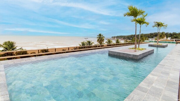 A clear pool with a view of the beach, surrounded by palm trees and a wooden deck. - Unity Cabo Branco Seafront by Carpediem (João Pessoa)