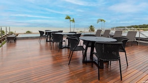 A wooden deck with outdoor seating, overlooking a beach and ocean. - Unity Cabo Branco Seafront by Carpediem (João Pessoa)