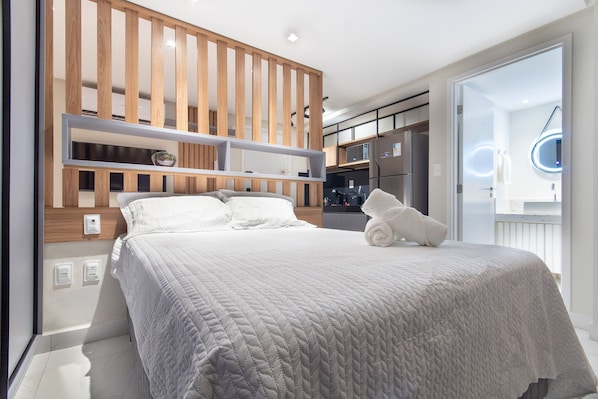 Een moderne slaapkamer met een groot bed, inbouwkasten van hout en uitzicht op de keuken en badkamer.
