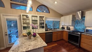 A kitchen with wooden cabinets, a granite countertop, a stainless steel range hood, and a large window.