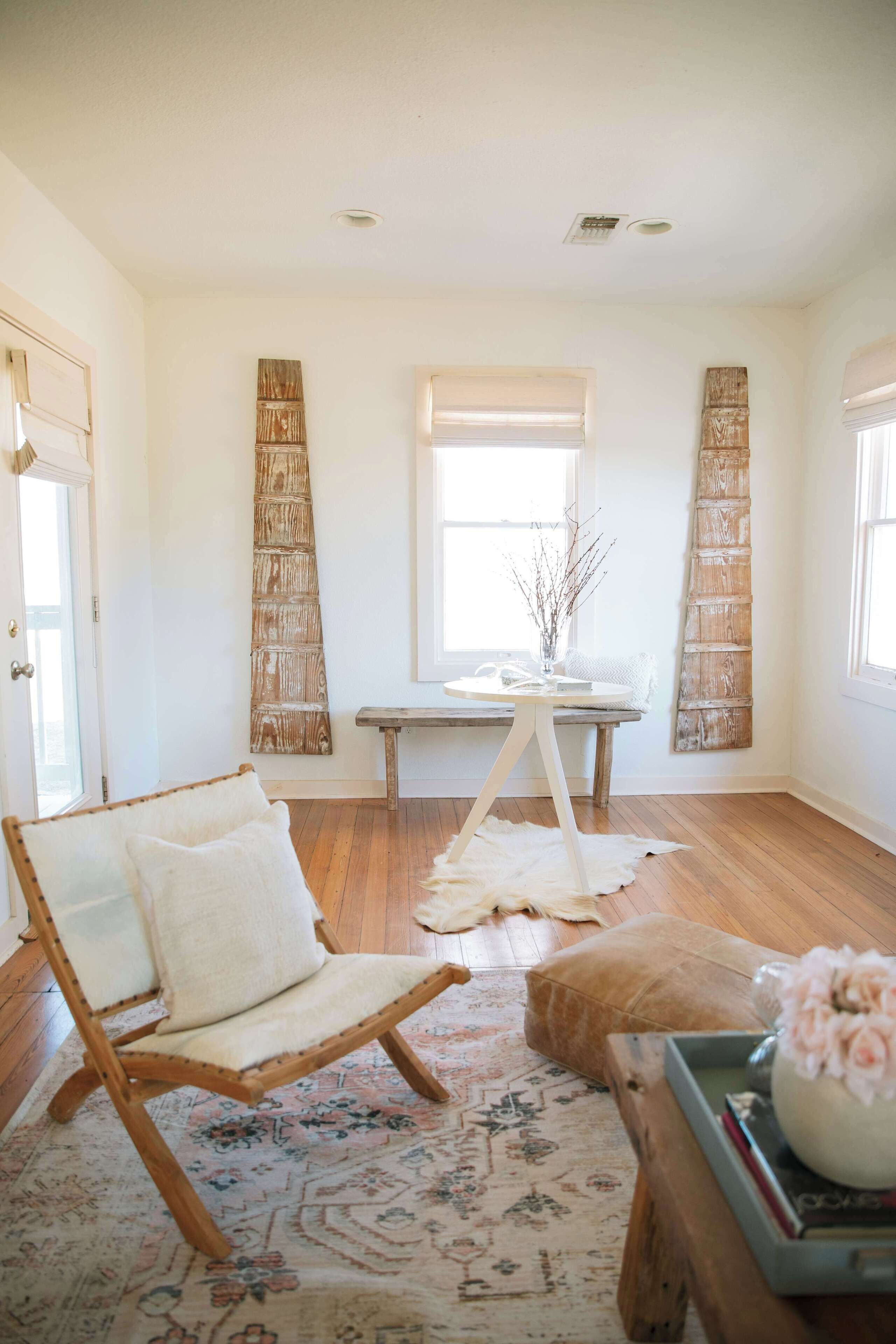A spacious room with a wooden floor, a large window, a wooden chair, a small round table, and a decorative wall piece.