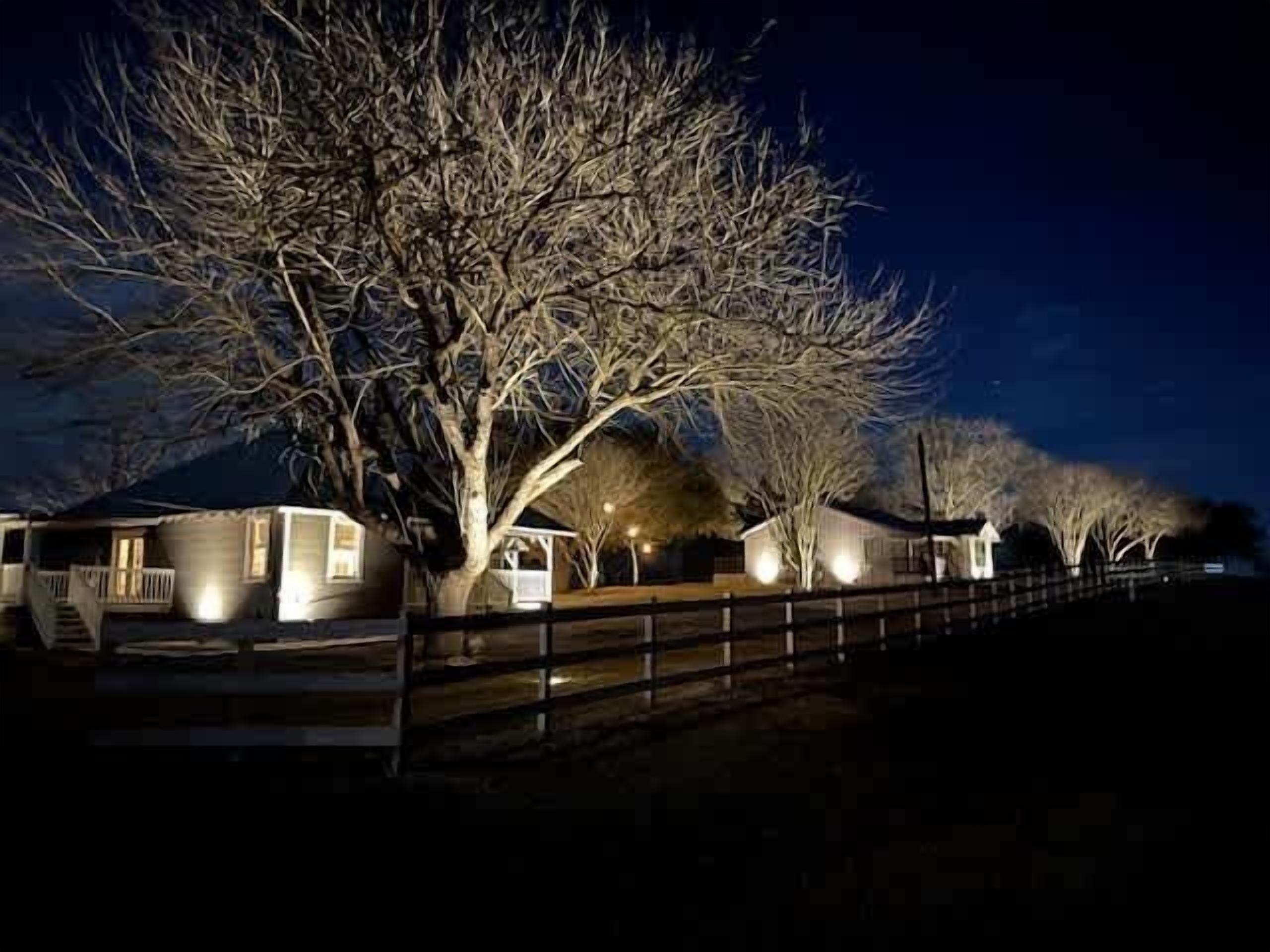 A row of cabins with a wooden fence in the foreground, illuminated by street lamps.