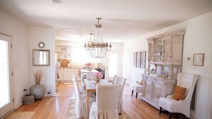 A spacious dining area with a wooden table, white upholstered chairs, and a chandelier. - NEW | Round Top Girls' Getaway | 2 BR w/ Fire Pit (Burton)