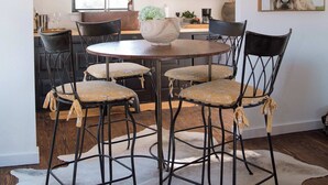 Een eetgedeelte met een ronde tafel, zwarte metalen stoelen, een houten plafondlamp en een koehuidtapijt.