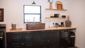 Een keuken met een groot raam, donkere kastjes, een houten aanrecht en diverse keukenbenodigdheden.