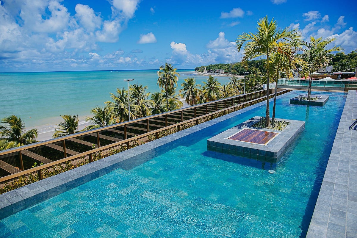 A pool with clear blue water, surrounded by palm trees and a beach view.