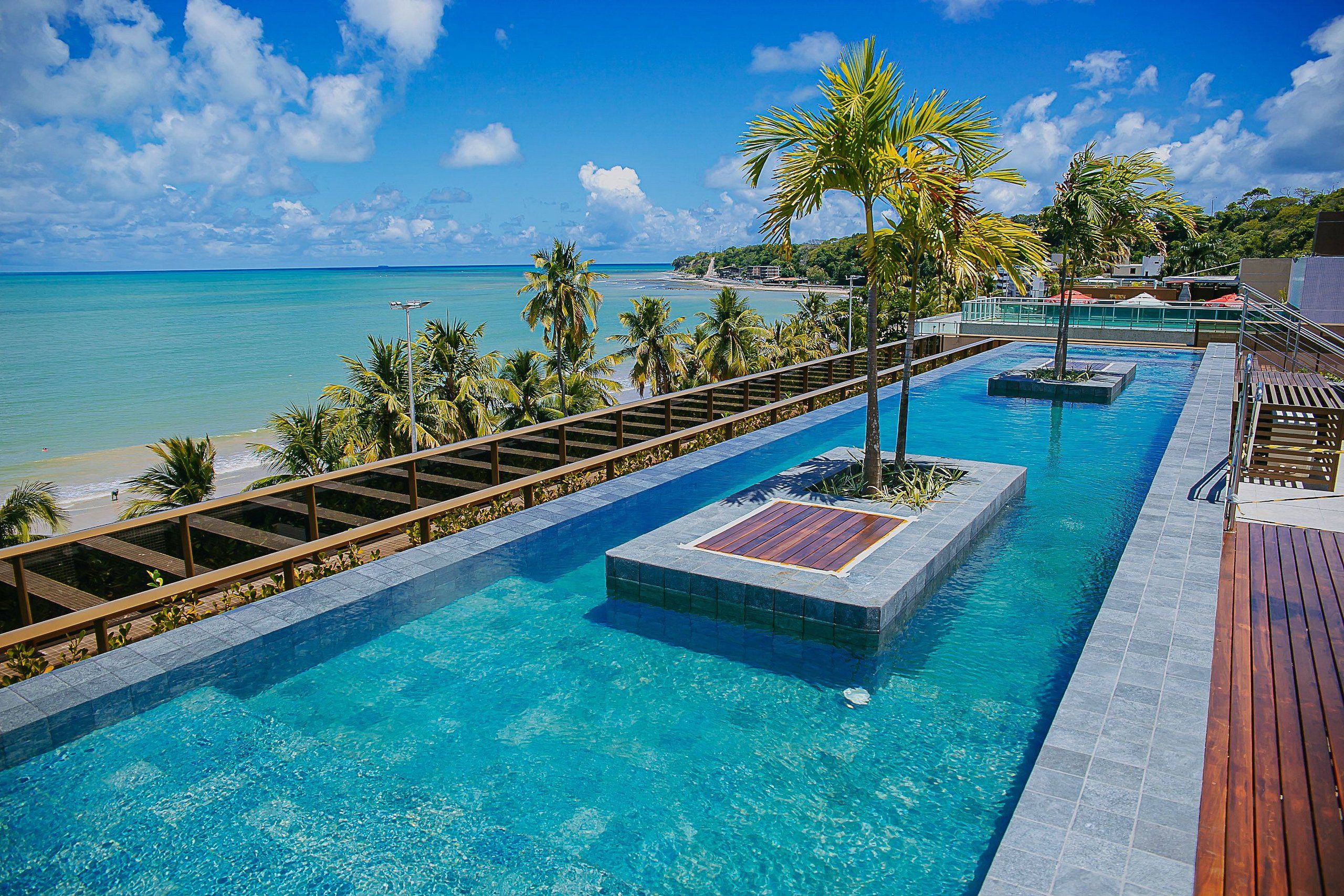 A pool with a wooden deck and a view of the beach.